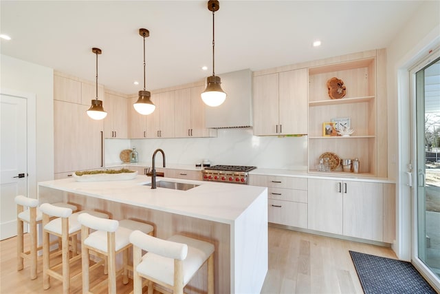 kitchen with sink, decorative light fixtures, light brown cabinets, light wood-type flooring, and a kitchen island with sink