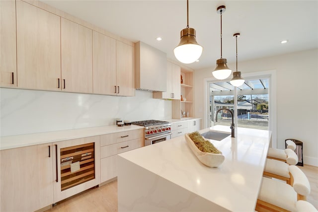 kitchen featuring stainless steel range, light brown cabinetry, light stone counters, and sink