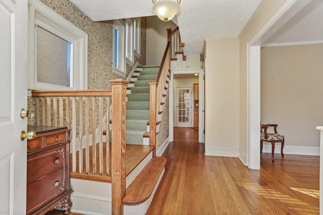 stairs with a textured ceiling, crown molding, and hardwood / wood-style floors