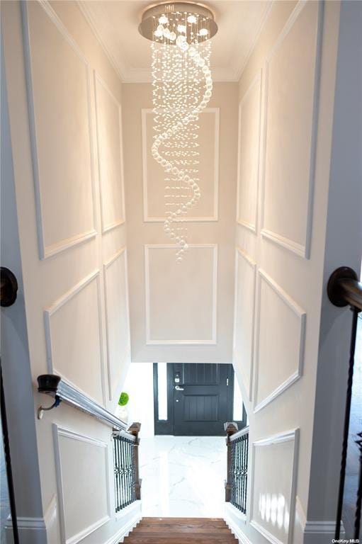 staircase with hardwood / wood-style flooring, ornamental molding, and an inviting chandelier