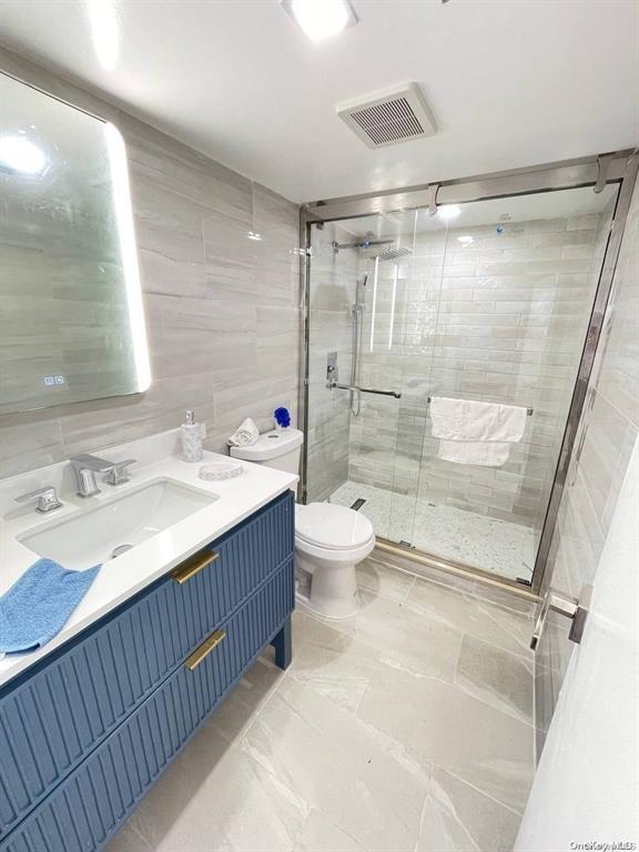 bathroom with vanity, toilet, tile walls, and a shower with shower door