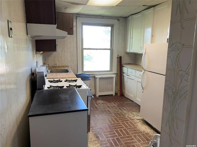 kitchen featuring electric range, radiator heating unit, sink, white fridge, and a paneled ceiling