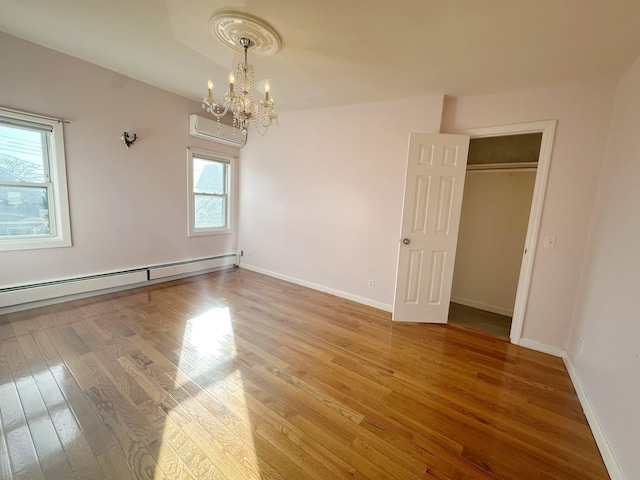 spare room featuring a chandelier, hardwood / wood-style floors, a wall unit AC, and a baseboard heating unit