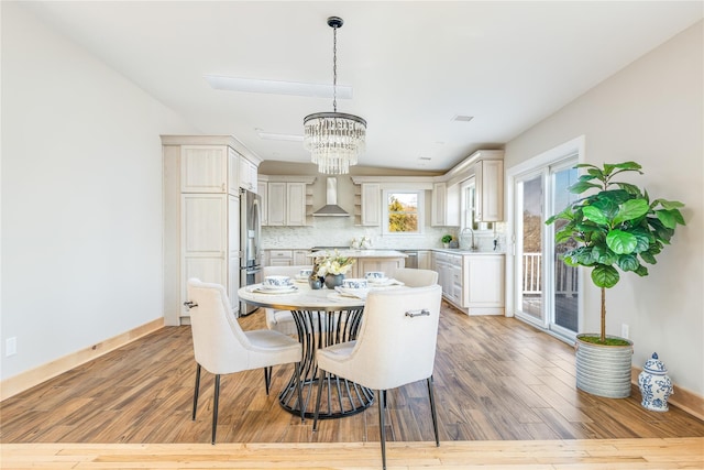 kitchen with decorative backsplash, pendant lighting, light hardwood / wood-style floors, and wall chimney range hood