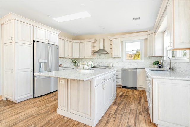 kitchen with appliances with stainless steel finishes, wall chimney exhaust hood, sink, a center island, and light hardwood / wood-style floors