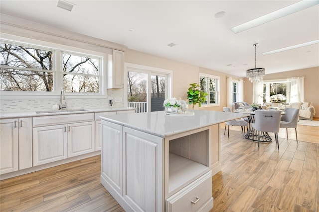 kitchen featuring sink, a center island, decorative light fixtures, and light wood-type flooring