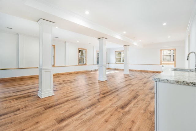 interior space featuring light wood-type flooring, ornate columns, crown molding, and sink