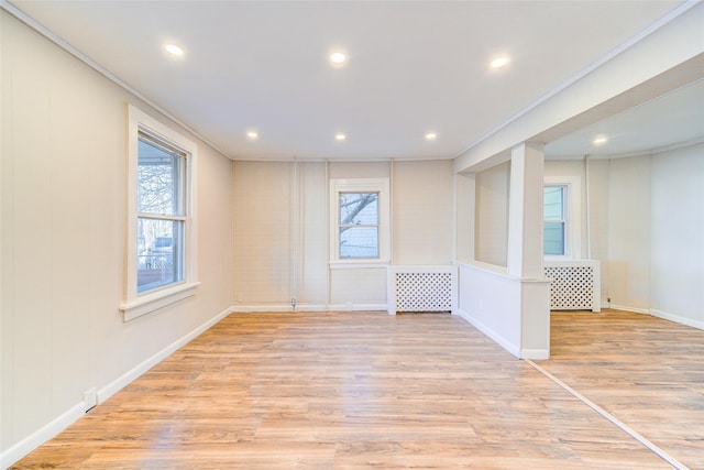 unfurnished room featuring radiator heating unit, ornamental molding, a wealth of natural light, and light hardwood / wood-style flooring