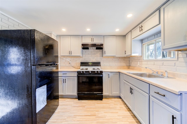 kitchen featuring backsplash, sink, black appliances, and light wood-type flooring