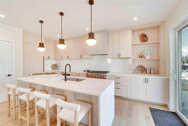 kitchen with light hardwood / wood-style floors, sink, hanging light fixtures, a kitchen island with sink, and light brown cabinets