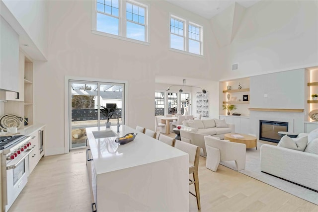 12 Depot Road 1302 (Pearl Way), Westhampton Beach, NY 11978 - dining area featuring built in features, light wood-style flooring, a high ceiling, and a glass covered fireplace