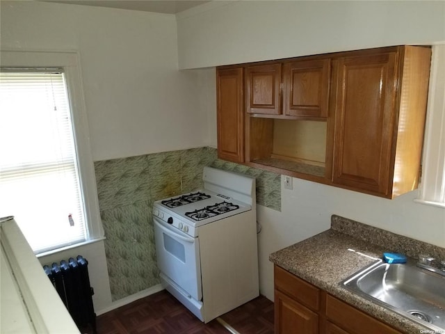 kitchen with dark parquet floors, tile walls, white gas range, and sink