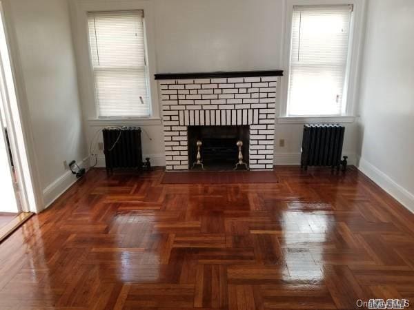 unfurnished living room featuring dark parquet floors, a brick fireplace, and radiator