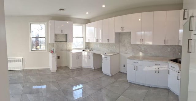 kitchen featuring white cabinets, radiator heating unit, backsplash, and sink