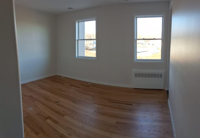 unfurnished room featuring radiator heating unit, light wood-type flooring, and a healthy amount of sunlight