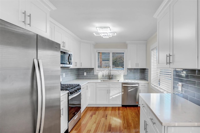 kitchen with white cabinets, sink, decorative backsplash, light wood-type flooring, and appliances with stainless steel finishes