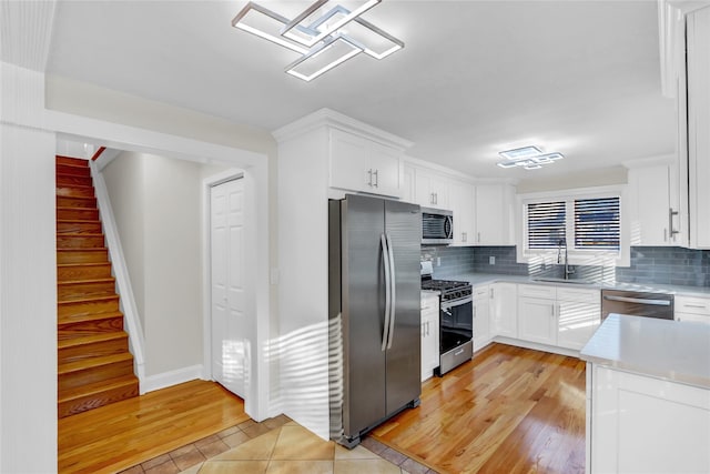 kitchen with white cabinets, light wood-type flooring, stainless steel appliances, and tasteful backsplash