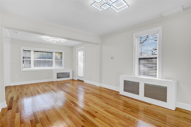 unfurnished living room with a notable chandelier, light wood-type flooring, and radiator heating unit