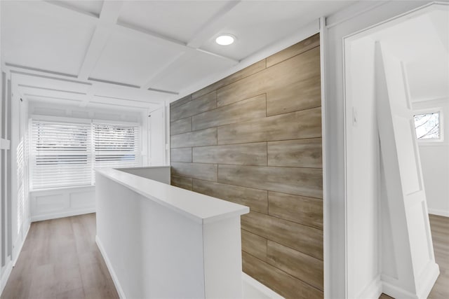 hallway featuring wood walls, beamed ceiling, coffered ceiling, and light wood-type flooring