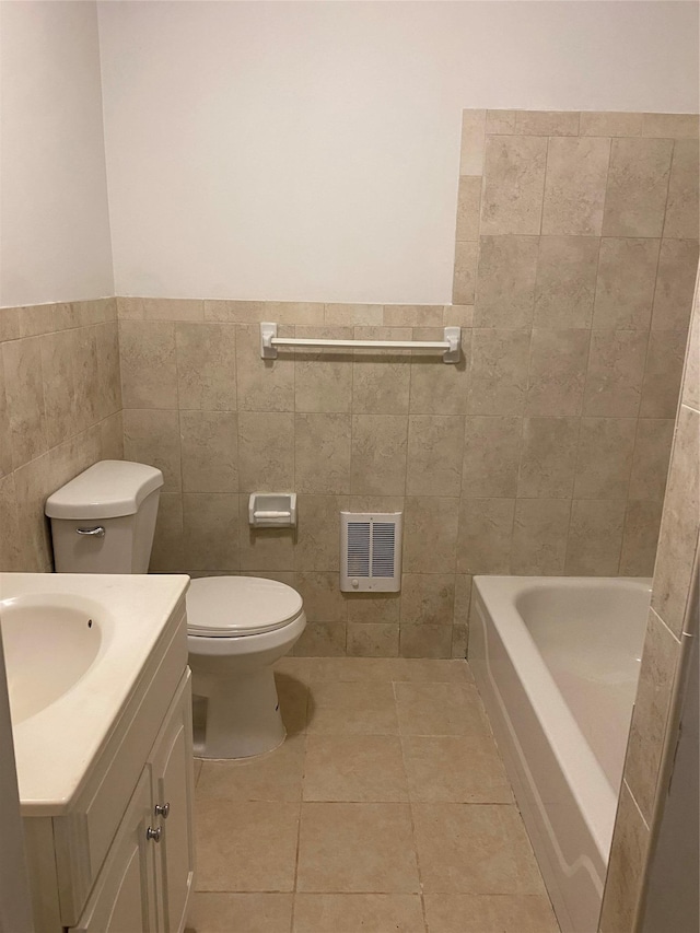 bathroom with tile patterned floors, toilet, a bathtub, vanity, and tile walls