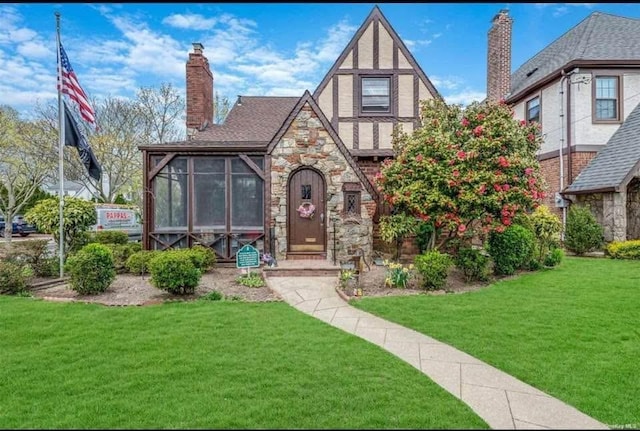 tudor-style house featuring a sunroom and a front yard