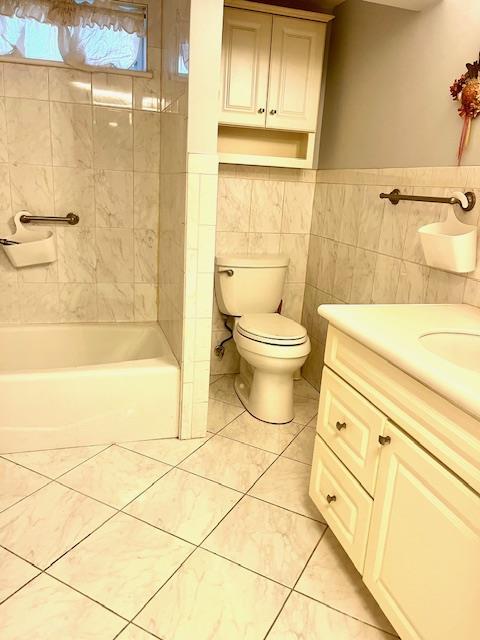 full bathroom featuring tiled shower / bath combo, tile patterned floors, toilet, vanity, and tile walls