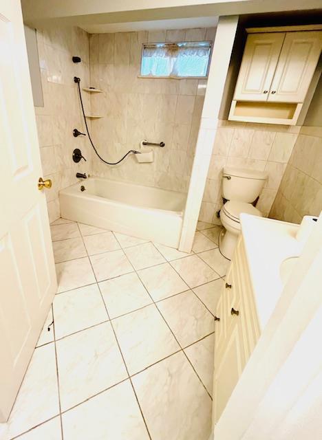 full bathroom with vanity, tile patterned floors, tiled shower / bath combo, toilet, and tile walls