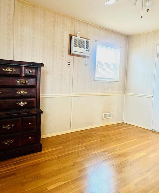 spare room featuring a wall mounted air conditioner, light hardwood / wood-style flooring, and ceiling fan