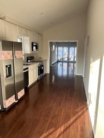 kitchen with lofted ceiling, white cabinets, backsplash, stainless steel appliances, and dark wood-type flooring