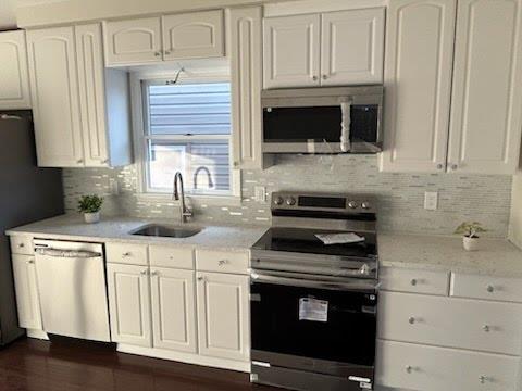 kitchen featuring sink, stainless steel appliances, light stone countertops, white cabinets, and decorative backsplash