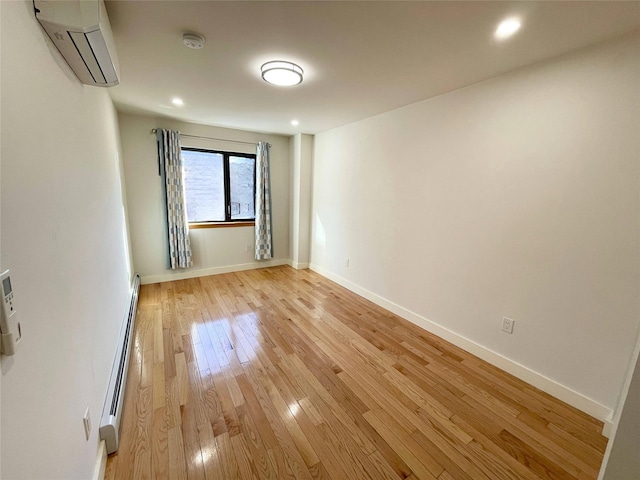 spare room with a baseboard radiator, a wall mounted AC, and light wood-type flooring