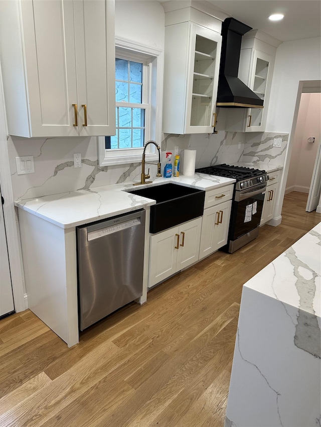 kitchen featuring light wood-type flooring, wall chimney range hood, sink, and appliances with stainless steel finishes