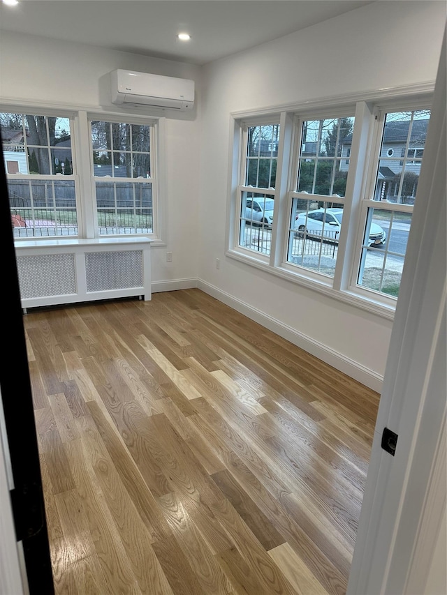 unfurnished dining area featuring radiator heating unit, light hardwood / wood-style floors, and an AC wall unit