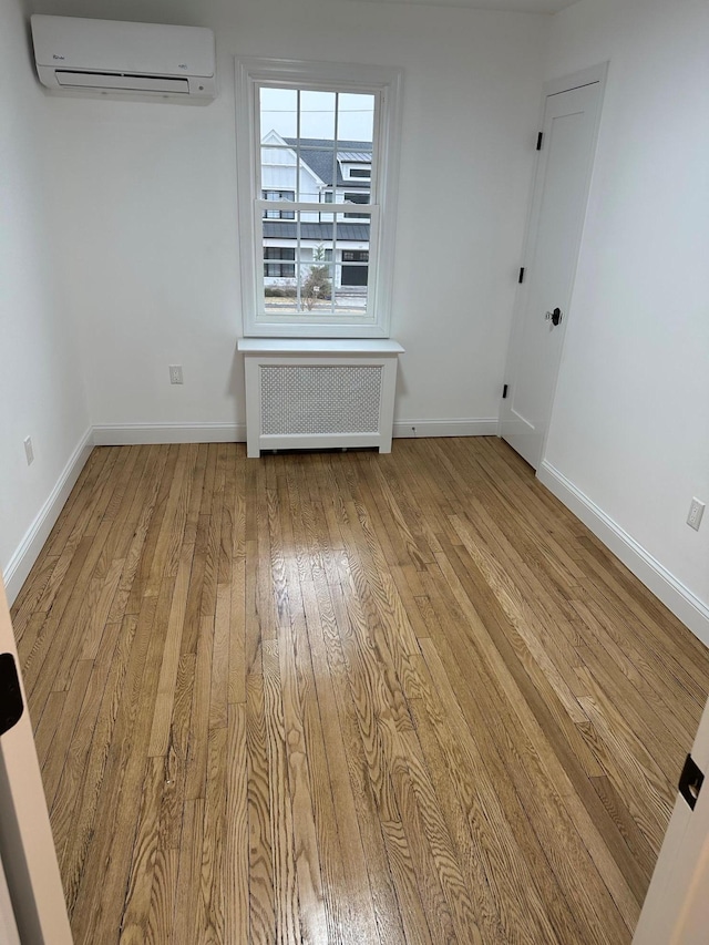 empty room featuring radiator, light hardwood / wood-style flooring, and a wall mounted air conditioner