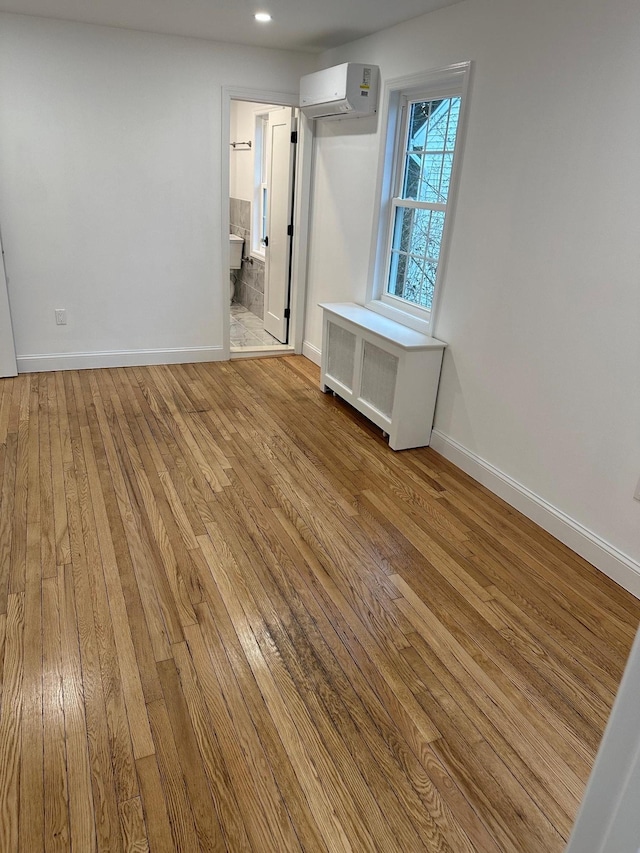 empty room featuring radiator, a wall mounted AC, and light wood-type flooring