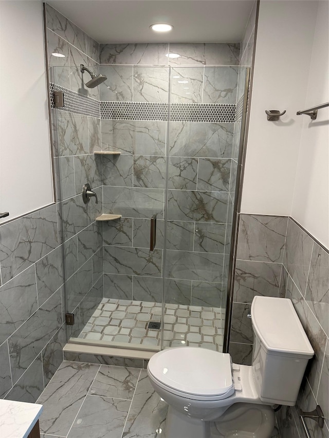 bathroom featuring a shower with door, vanity, tile walls, and toilet