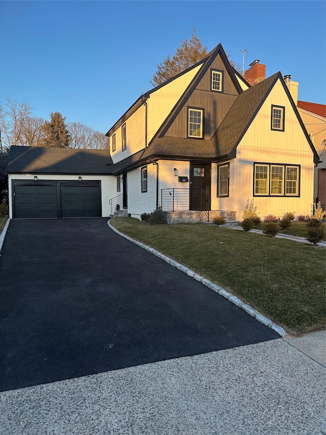 view of front of property with driveway, a chimney, roof with shingles, an attached garage, and a front lawn