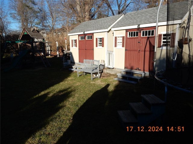 view of outbuilding featuring a trampoline, a playground, and a lawn