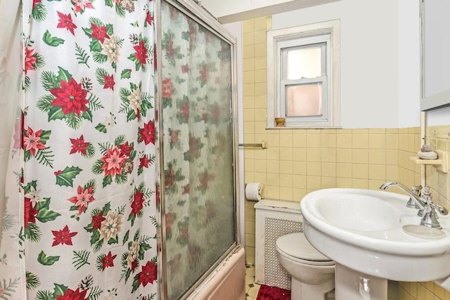 full bathroom with shower / bath combination with glass door, radiator, sink, tile walls, and toilet