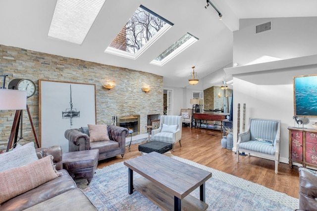 living room with hardwood / wood-style flooring, vaulted ceiling with skylight, a fireplace, and track lighting