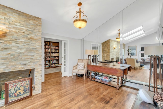 interior space featuring built in shelves, a stone fireplace, wood-type flooring, and lofted ceiling