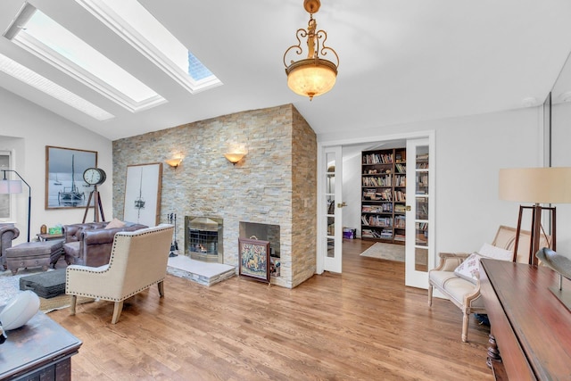 living room with vaulted ceiling with skylight, a stone fireplace, and light wood-type flooring