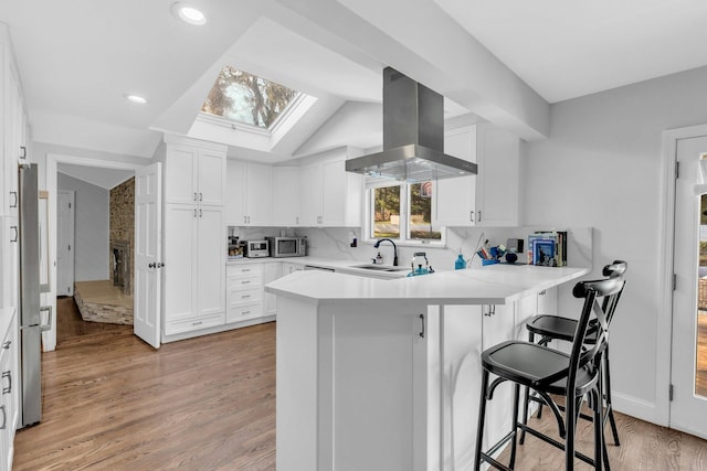 kitchen with white cabinetry, ventilation hood, kitchen peninsula, a kitchen bar, and vaulted ceiling with skylight