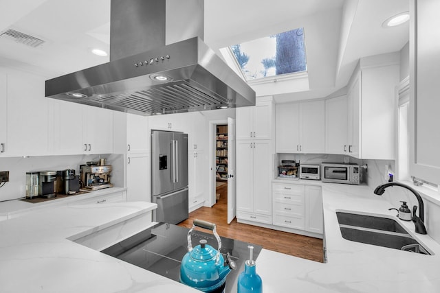 kitchen featuring wall chimney range hood, sink, light stone countertops, appliances with stainless steel finishes, and white cabinetry