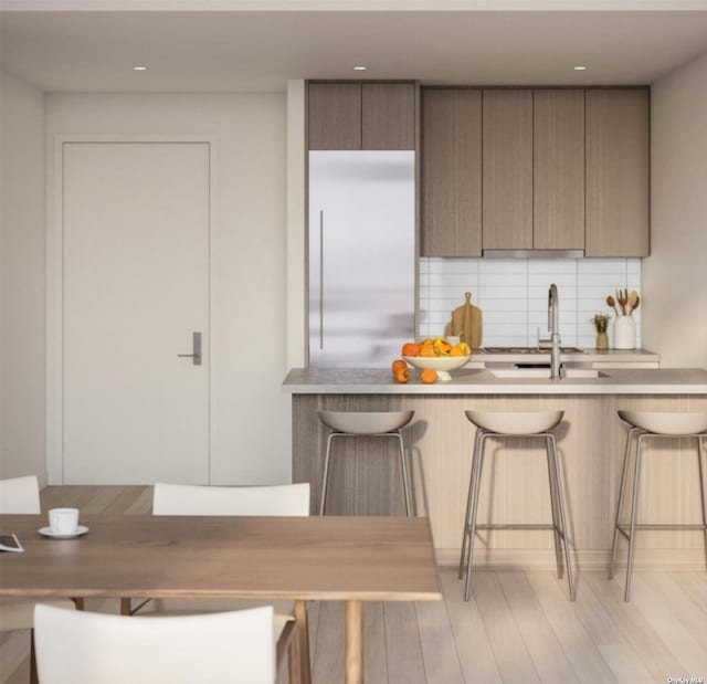 kitchen with light wood-type flooring, tasteful backsplash, a breakfast bar, sink, and stainless steel built in fridge