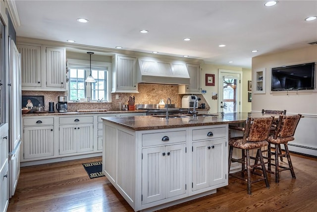 kitchen with premium range hood, white cabinets, a kitchen island with sink, and pendant lighting