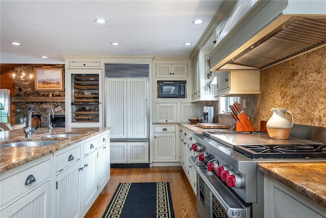 kitchen with hardwood / wood-style floors, exhaust hood, built in appliances, decorative backsplash, and sink