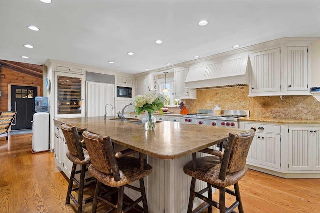 kitchen with white cabinetry, a center island with sink, and custom exhaust hood