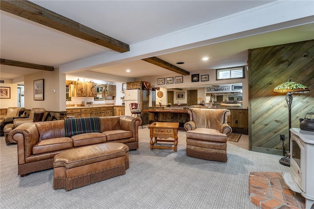 living room with light colored carpet, a wood stove, beam ceiling, and wooden walls