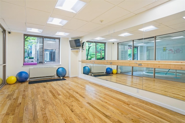 exercise area with a paneled ceiling, a healthy amount of sunlight, and hardwood / wood-style floors